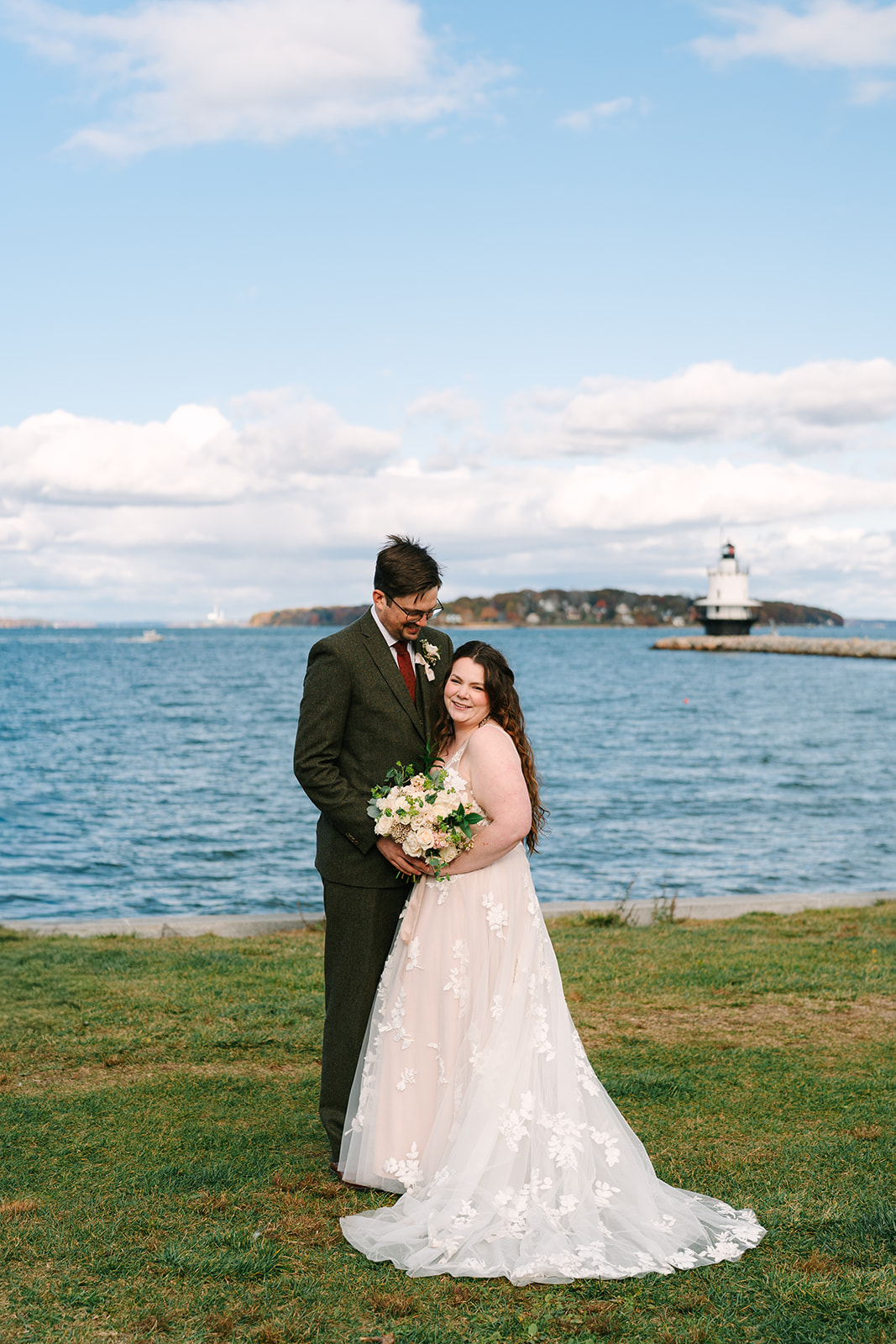 A couple hugs in front of a light house while eloping in Portland, Maine.
